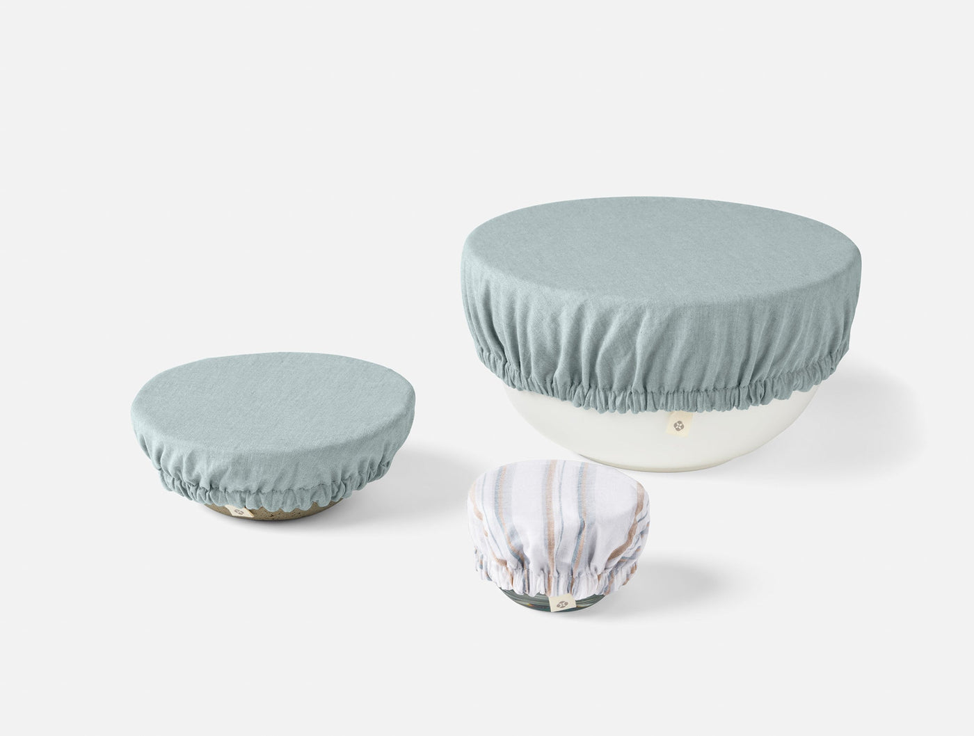 Three Coyuchi Conserve bowl covers in sage and floral print, shown in small, medium, and large sizes.