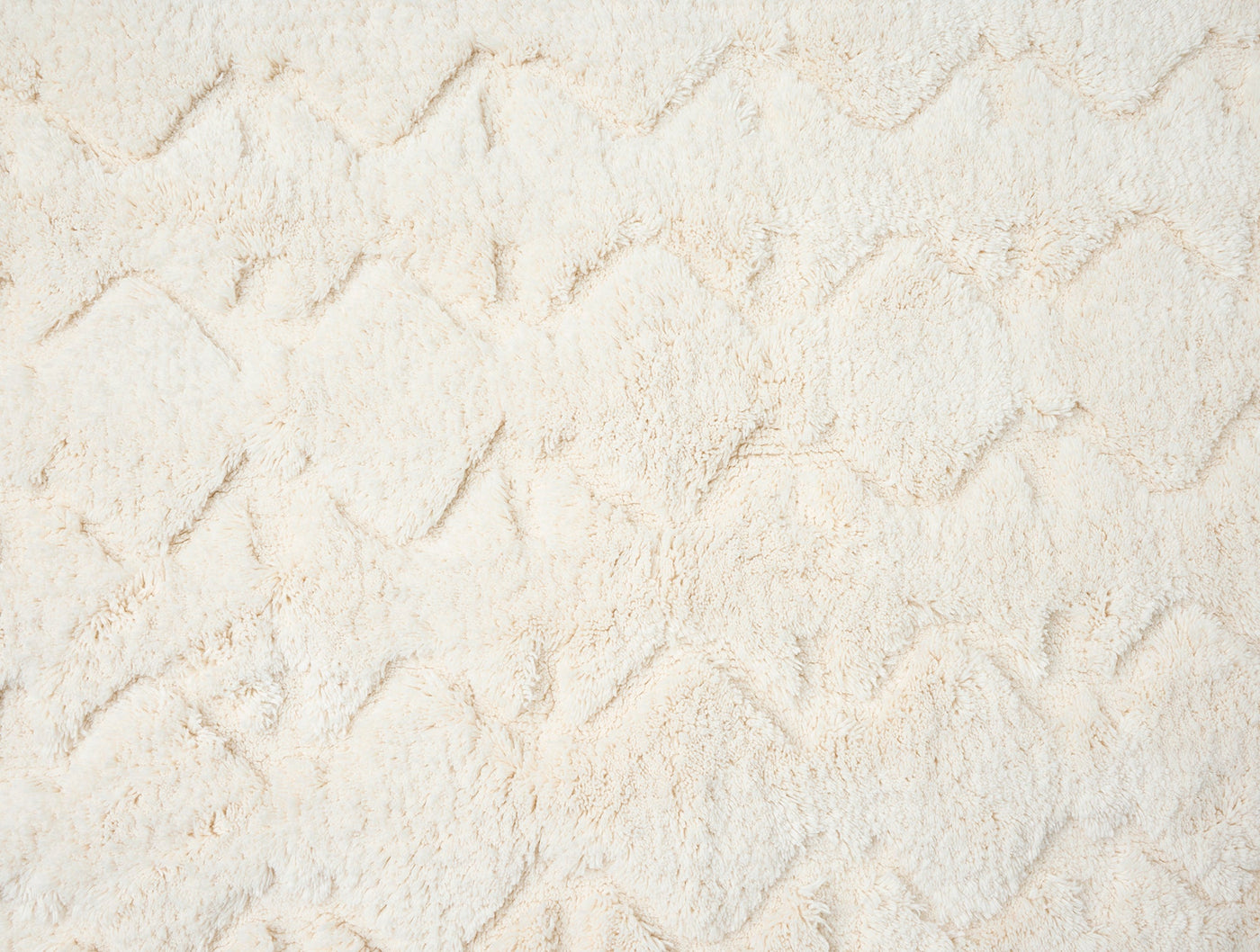 Close-up of ivory tufted cotton bath rug with raised diamond chevron texture pattern.