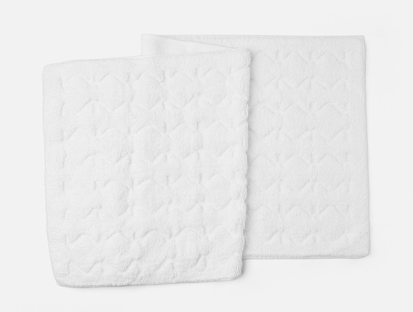 Two white Coyuchi Diamond Shag bath rugs with quilted diamond texture, overlapping on gray background.