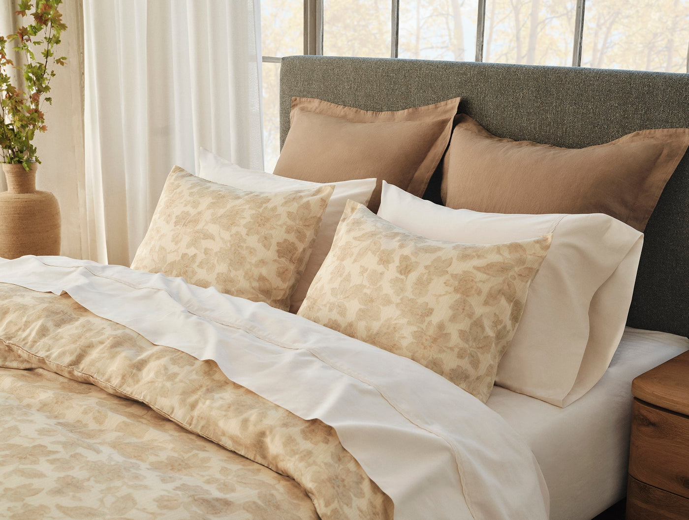 White sateen sheet set styled on a bed with floral-print pillows and neutral bedding.