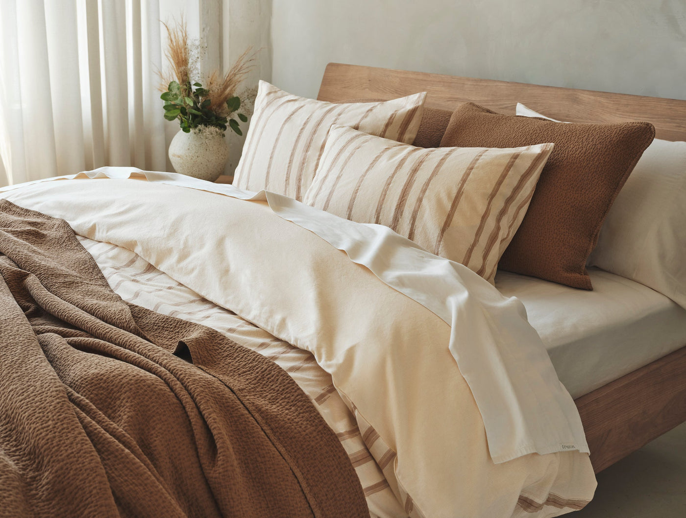 Cazadero Stripe duvet cover in ivory, styled on bed with warm caramel accent pillows and throw.