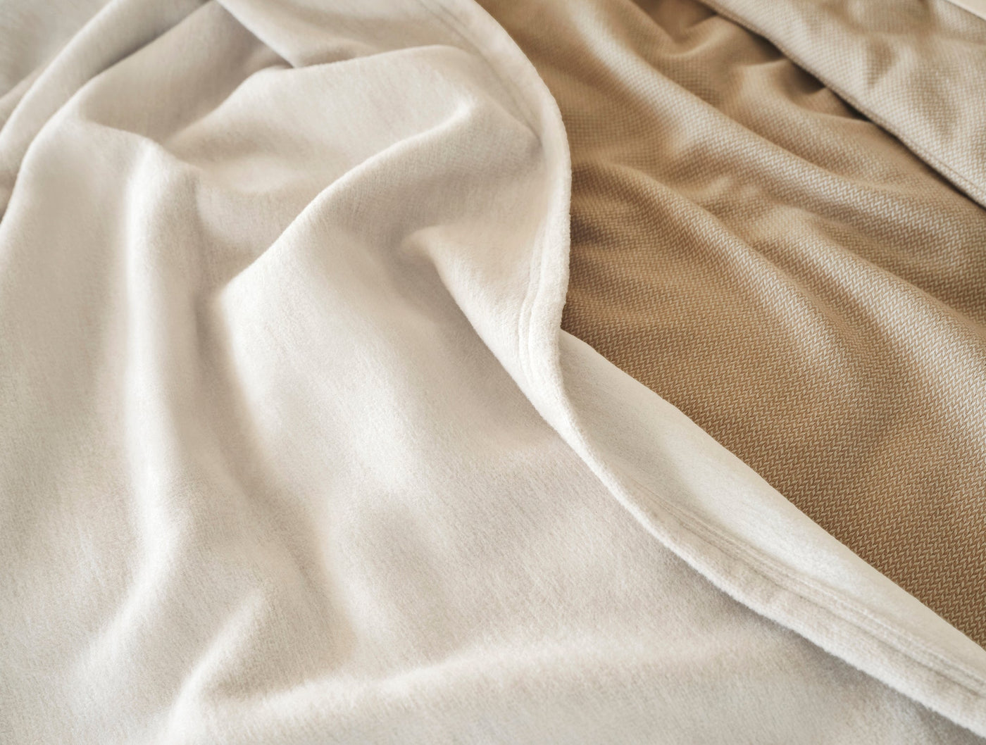 Ivory cotton throw draped over a camel waffle-weave blanket, close-up of fabric textures.