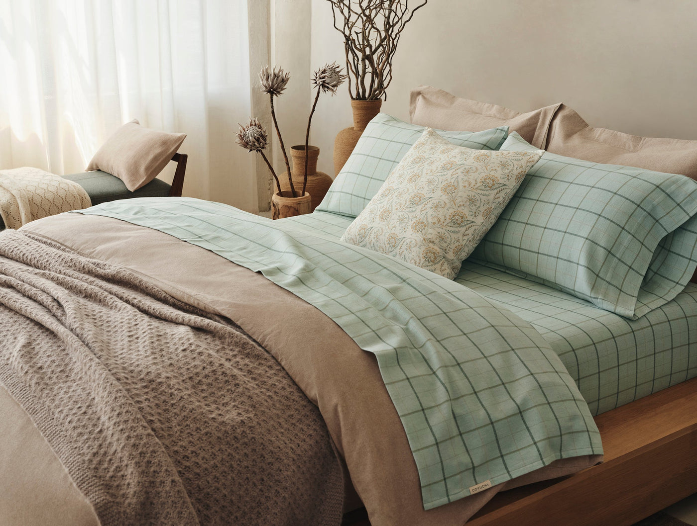 Sage green plaid flannel pillowcases styled on a made bed with neutral bedding.