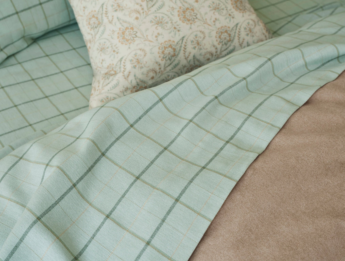 Close-up of Coyuchi Cloud Brushed Flannel in seafoam green windowpane plaid, draped on a bed.