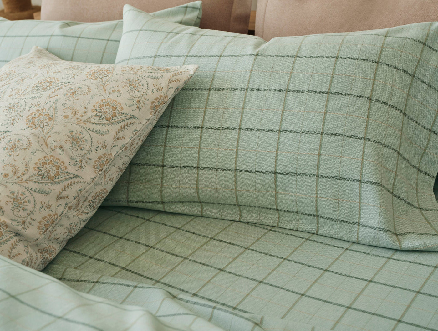 Sage green flannel sheet set with grid plaid pattern, styled on a bed with a floral accent pillow.