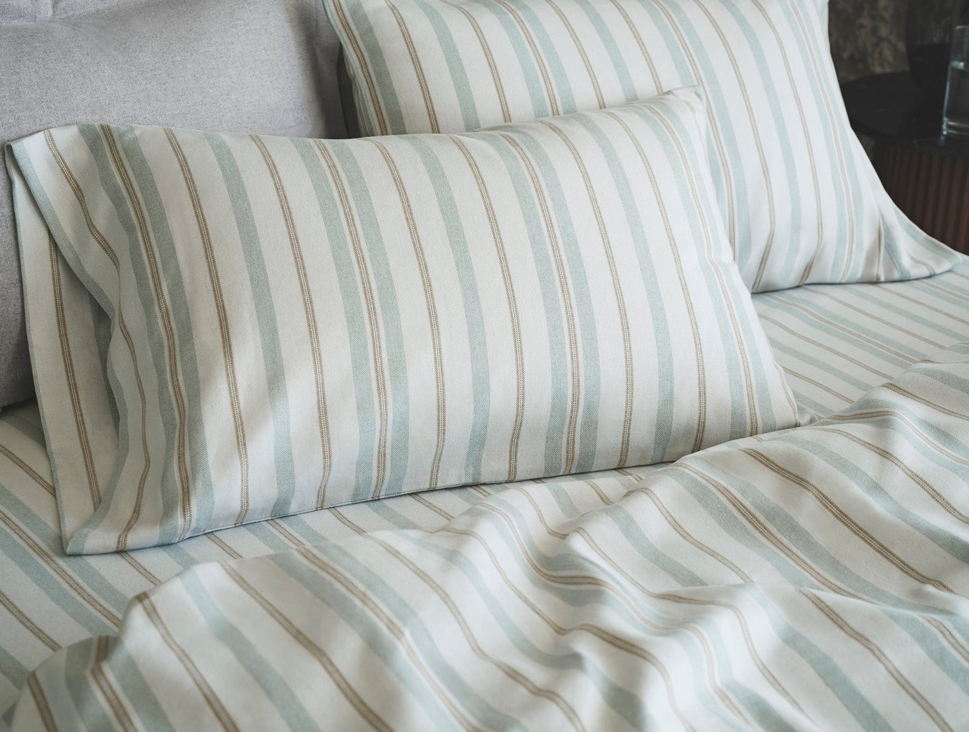 Close-up of Coyuchi Cloud Brushed Flannel pillowcases in soft aqua and tan stripes on a made bed.