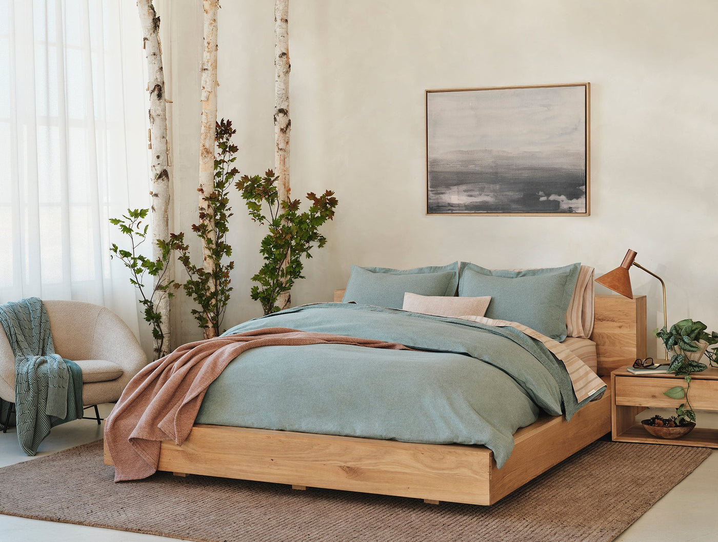 Sage green flannel shams on a made bed with dusty rose throw, natural wood frame.