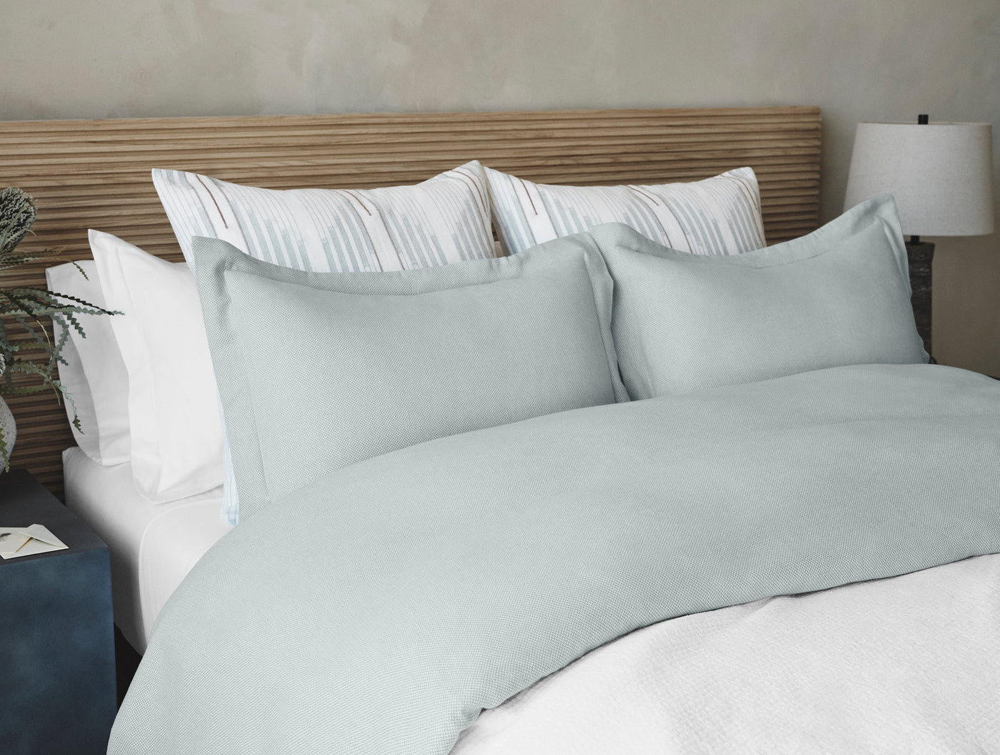 Duvet cover and shams in soft seafoam, layered with white striped pillows on a wood headboard.