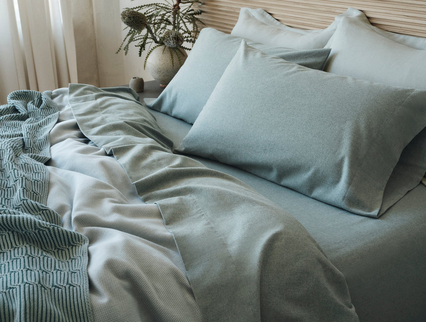 Coyuchi Cloud Brushed Flannel pillowcases in sage green styled on a made bed.