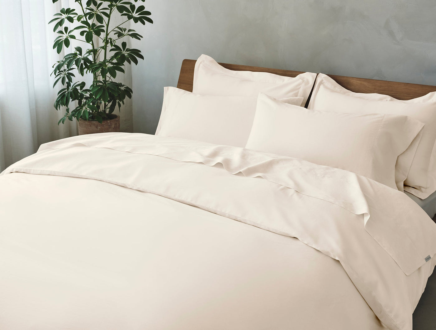 Ivory sateen sheet set styled on a made bed with layered pillows and a potted plant nearby.