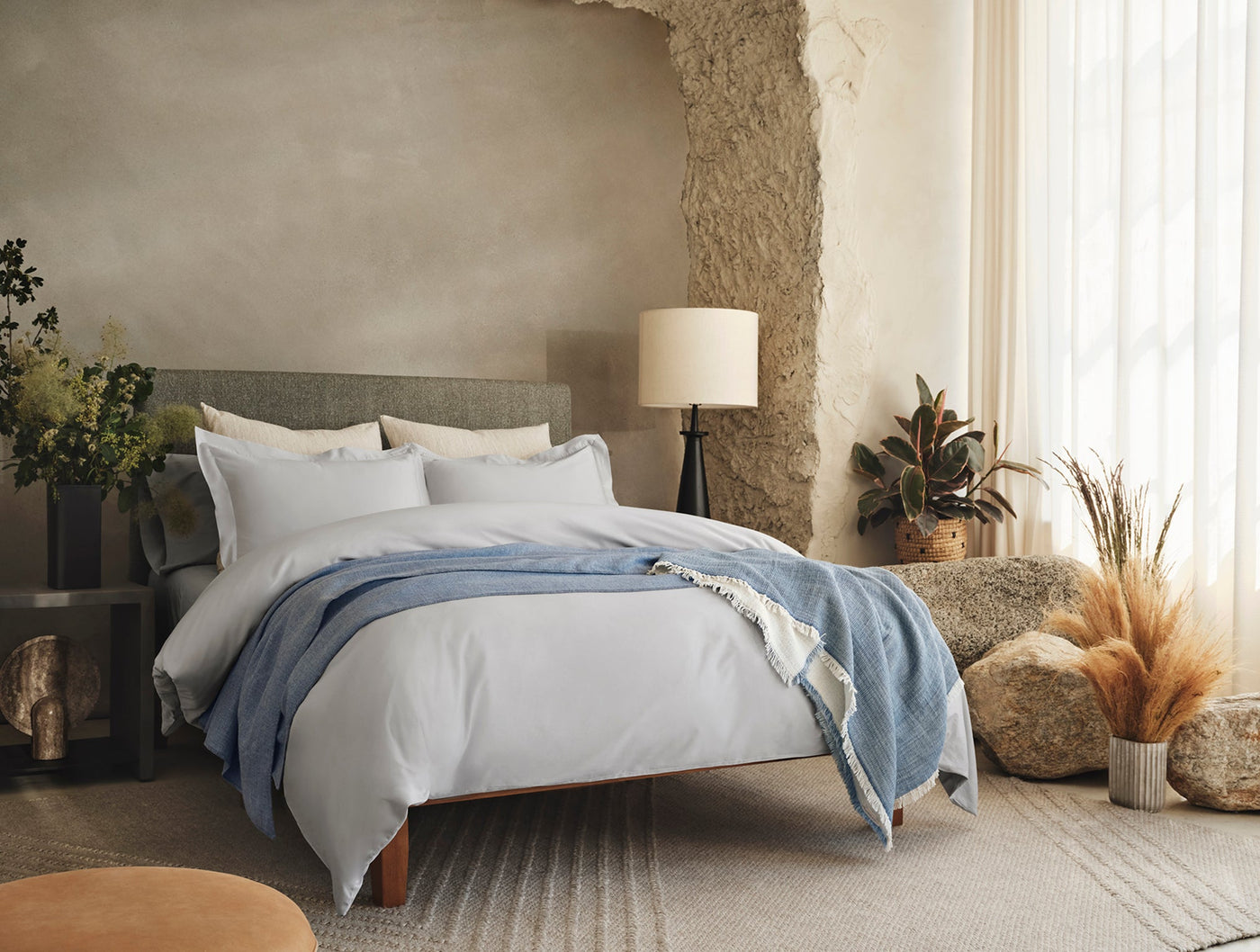 Styled bedroom with white Coyuchi sateen sheet set, blue throw draped across bed, natural textures throughout.