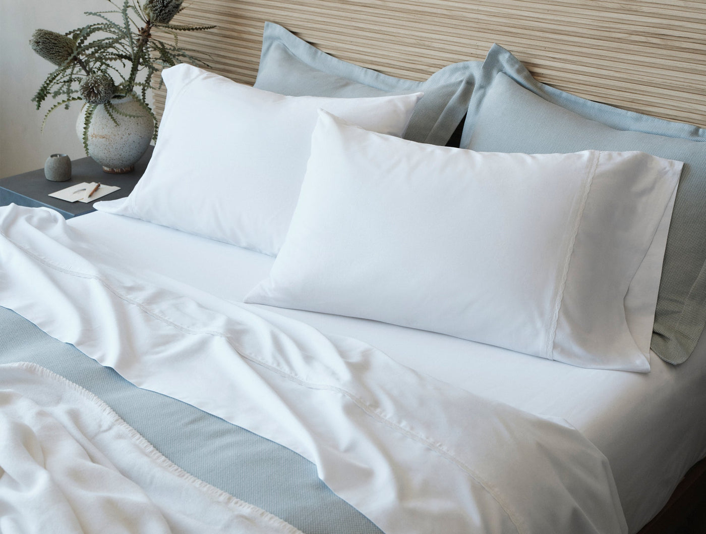 Close-up of white Coyuchi Cloud Soft Sateen pillowcases styled on a bed with blue-grey bedding.
