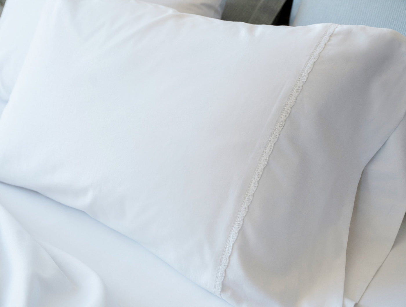 Close-up of white Coyuchi Cloud Soft Sateen pillowcase hem detail on a made bed.