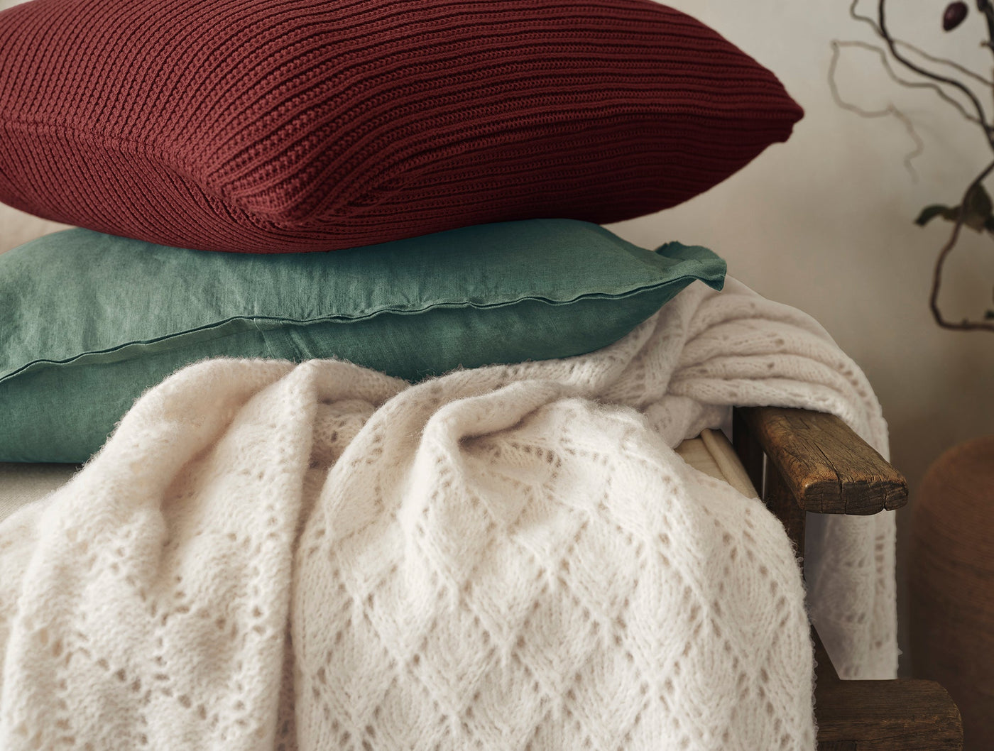 Ivory alpaca-cotton knit throw draped over bench, styled with crimson and teal cushions.