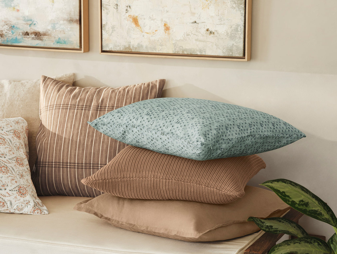 Coyuchi Coral Bell Print pillow styled with neutral striped and solid pillows on a white bench.