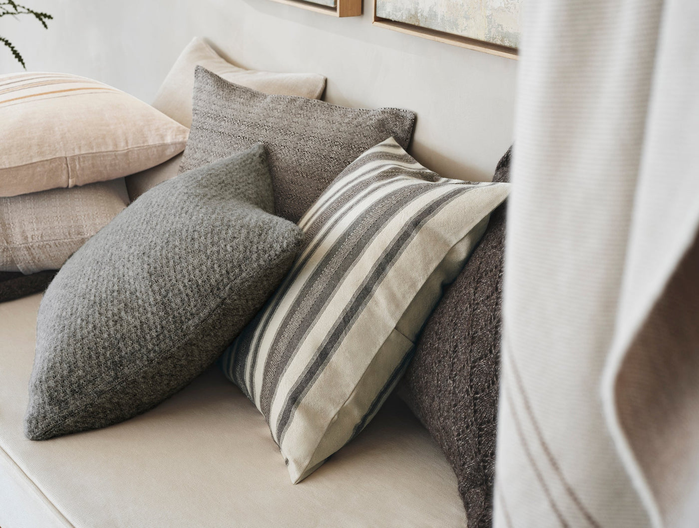 Coyuchi Serrano pillow styled with mixed-texture cushions in grey and natural tones on a sofa.