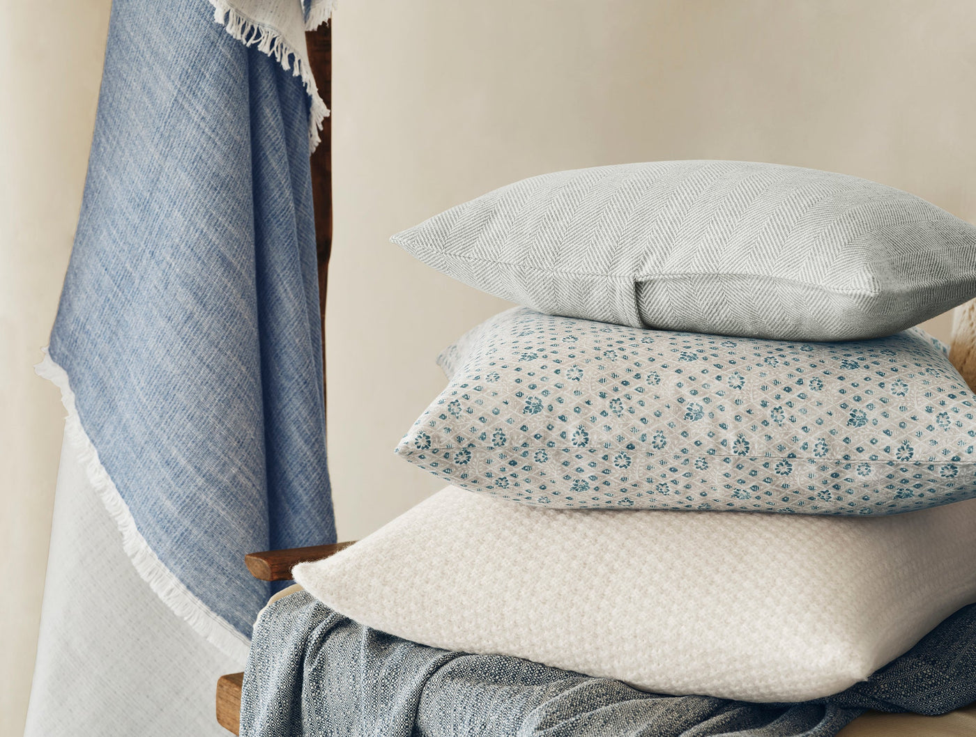 Stack of blue and white textured pillows with fringed denim throw on wooden ladder.