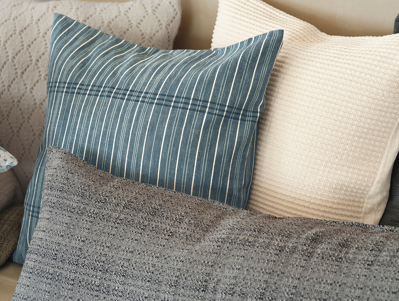 Coyuchi Marshall pillow in slate blue stripe, styled with neutral textured cushions on a sofa.