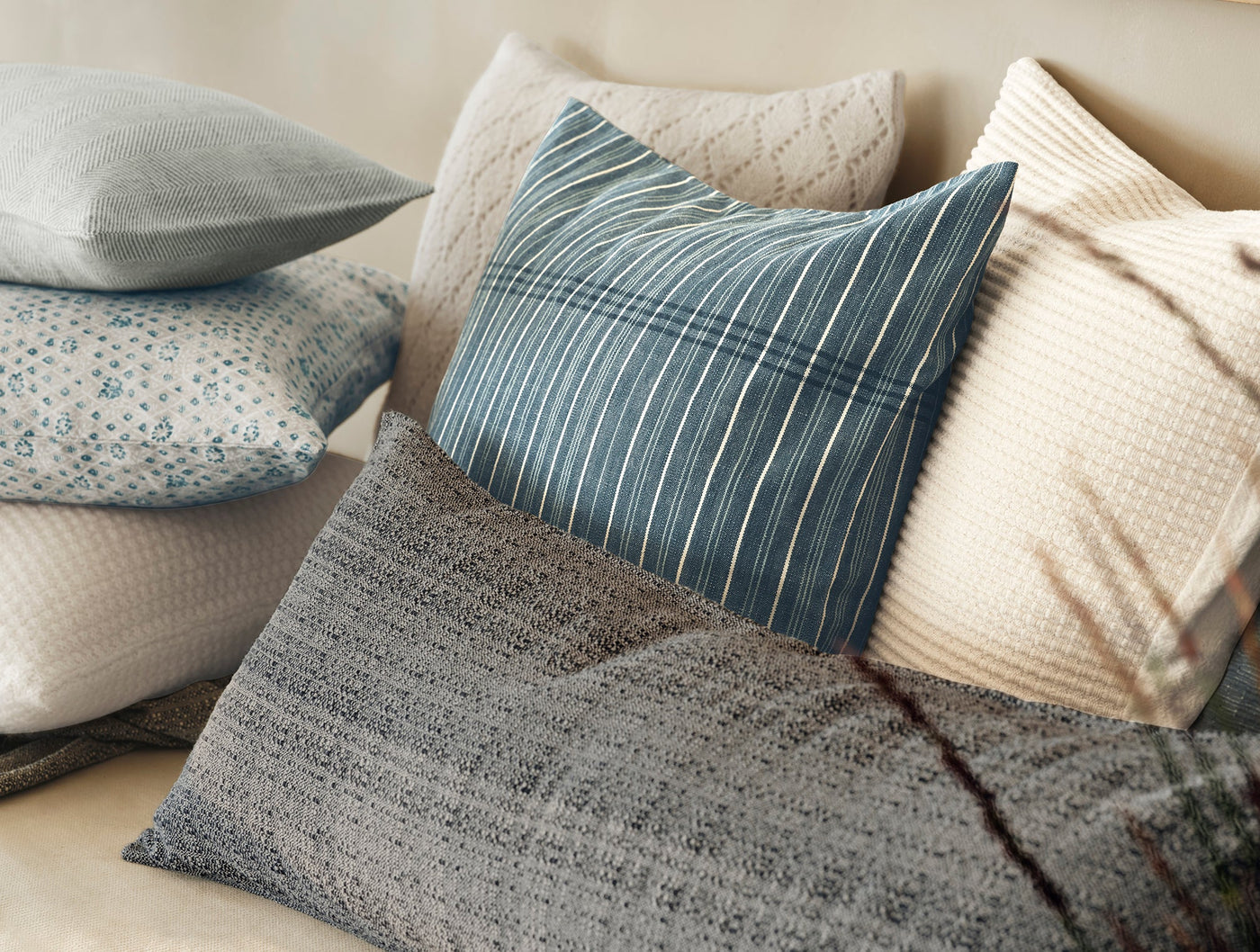 Close-up of Coyuchi Lido pillow in teal stripe among layered blue and ivory cushions.