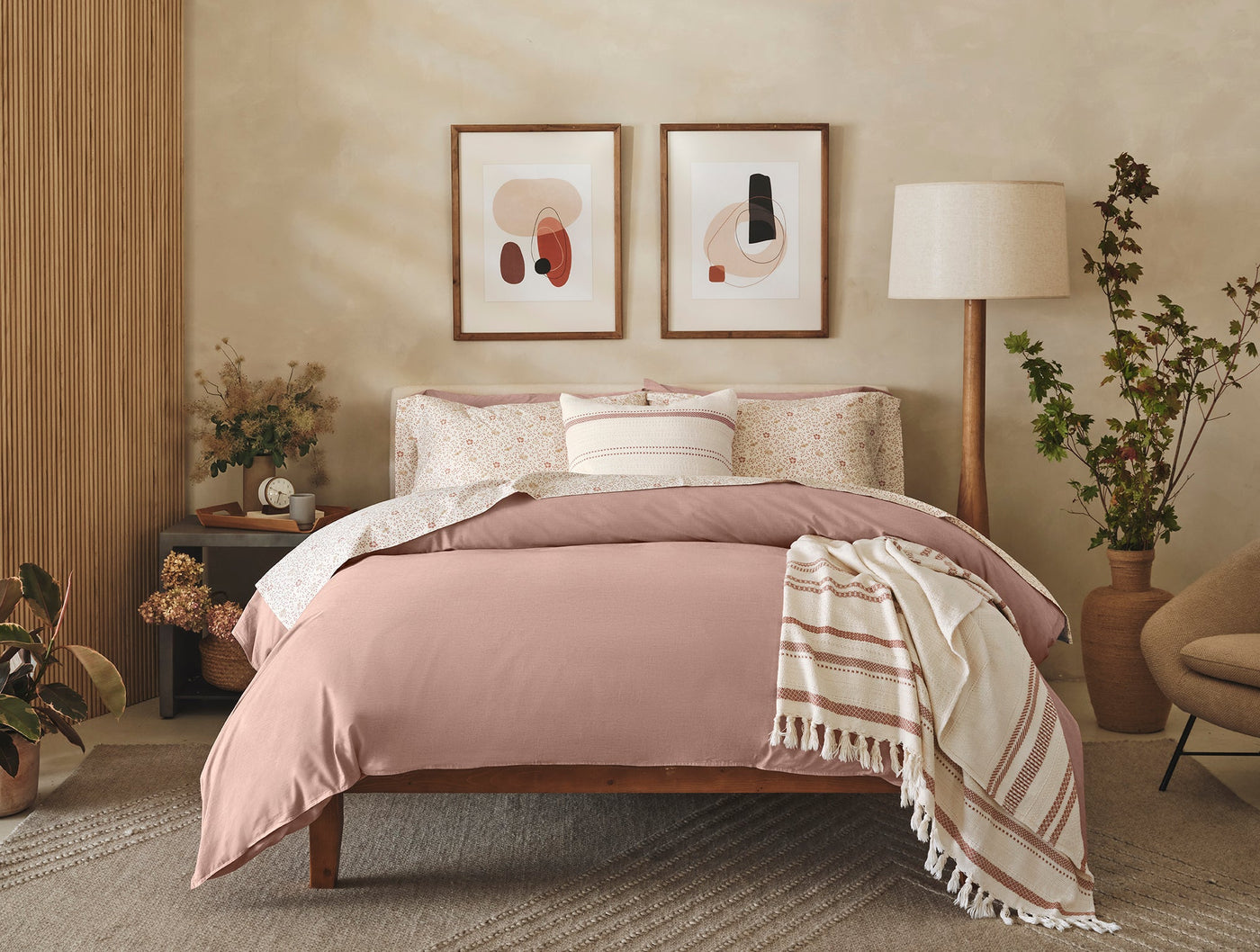 Dusty rose duvet and floral-print percale sheets styled on a wood bed in a warm neutral bedroom.