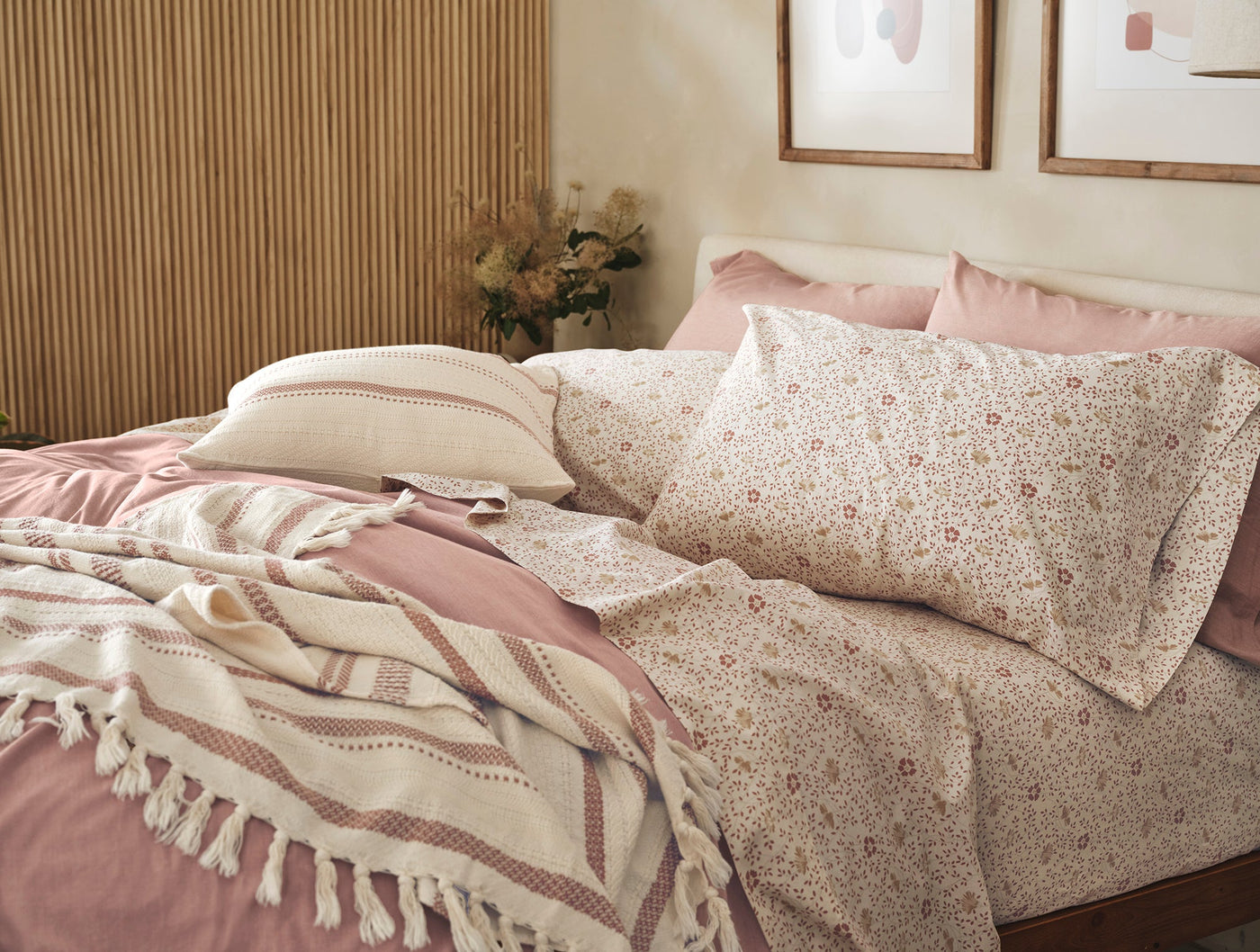 Floral print percale sheet set styled on bed with blush pillowcases and fringed throw.