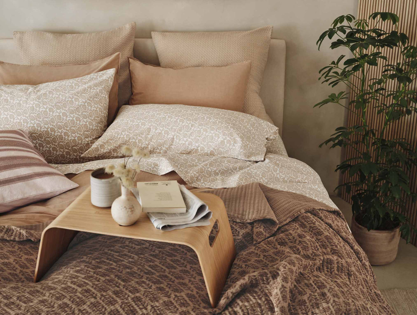 Styled bed scene with mocha floral percale pillowcases layered with warm earth-tone bedding.