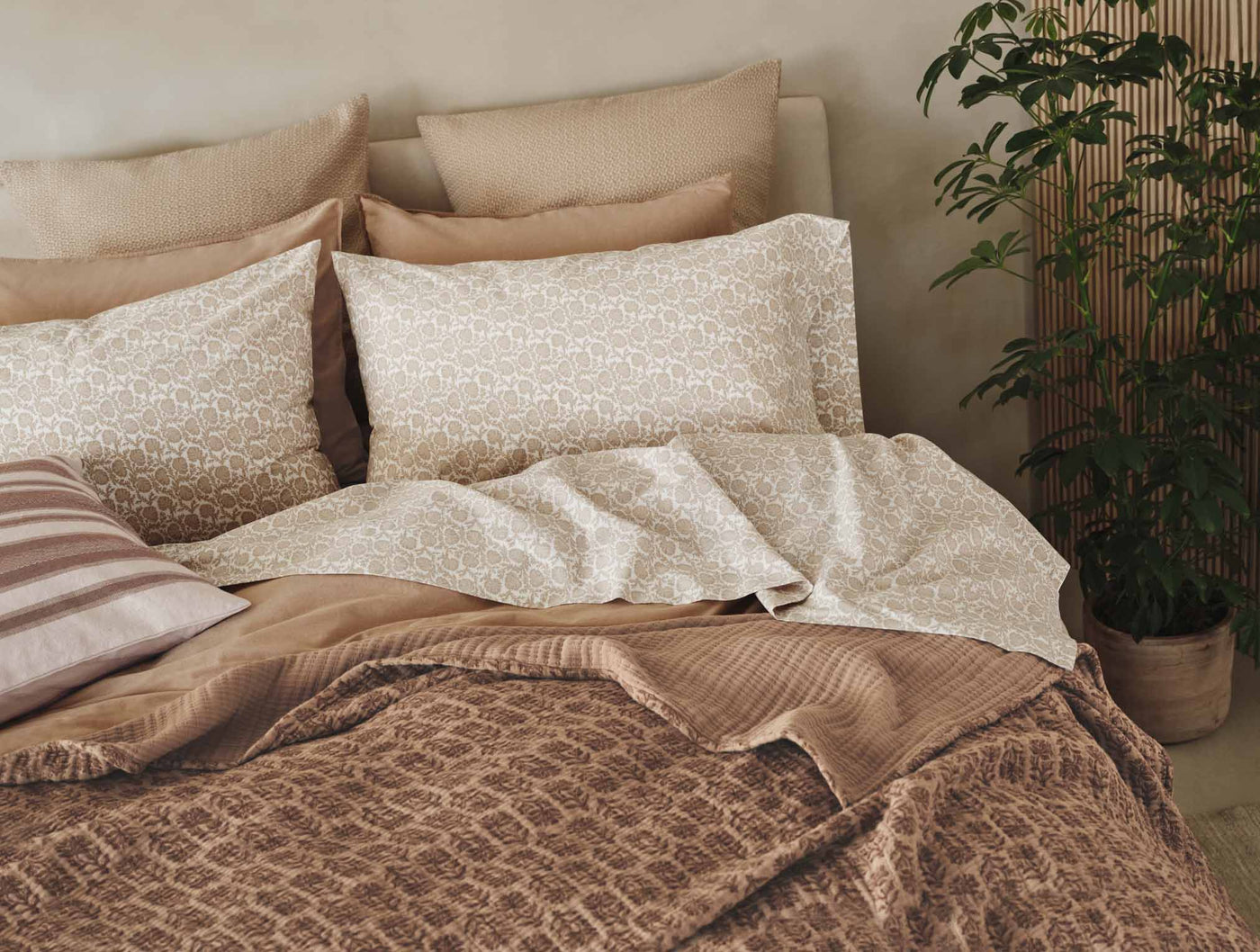 Close-up of Coyuchi Print Percale sheet set in warm taupe tones styled on a bed.