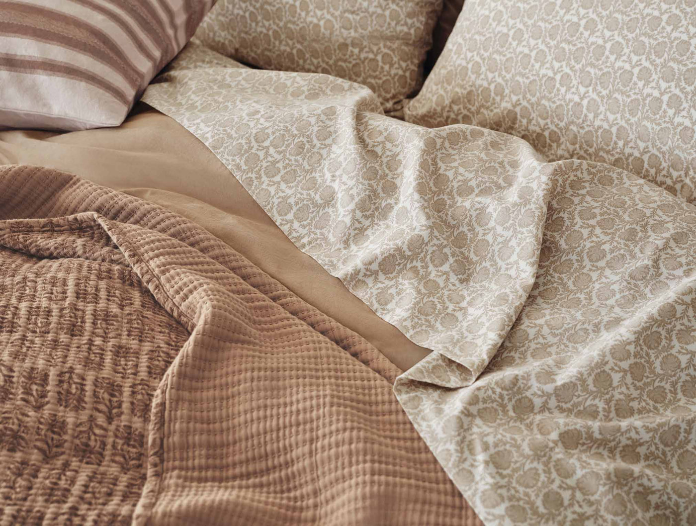 Sage floral print percale sheet set draped over bed with waffle-knit throw accent.