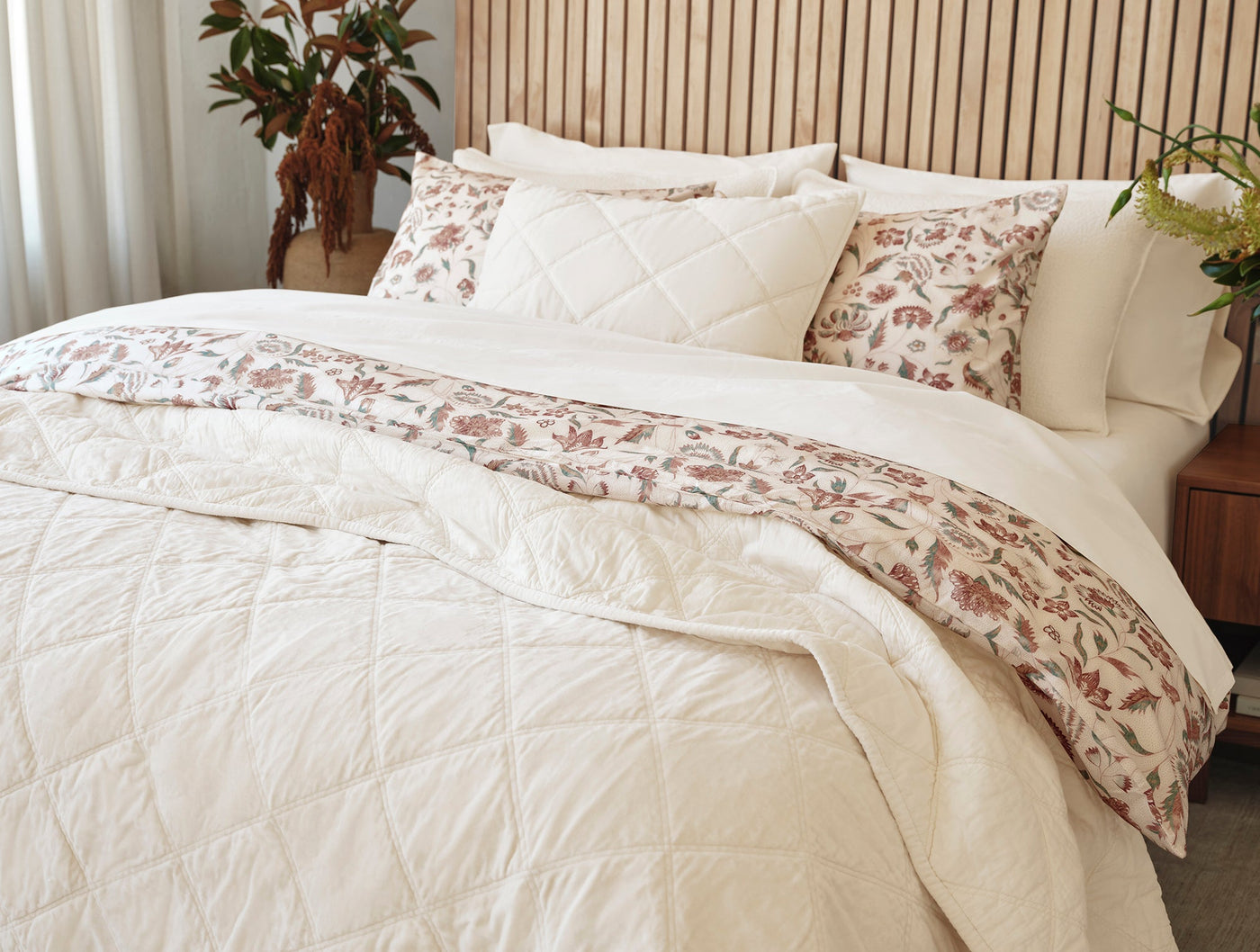 Ivory quilted bedspread styled with floral block-print shams on a made bed.