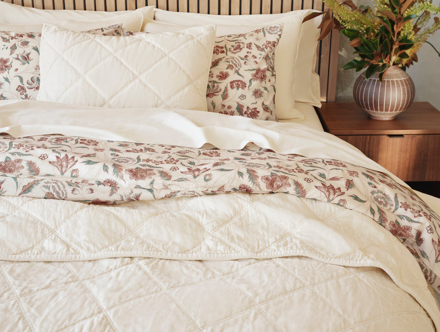 Ivory quilted diamond-stitched bedding styled with floral accent pillows on a made bed.