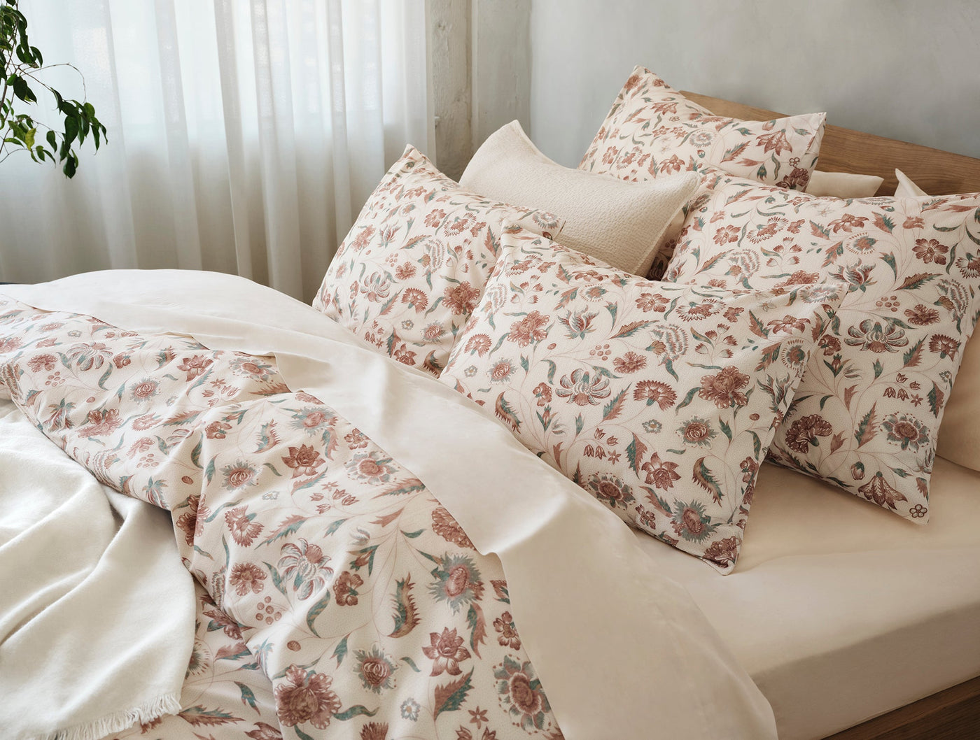 Duvet cover and pillowcases with terracotta and sage floral print on ivory, styled on a bed.