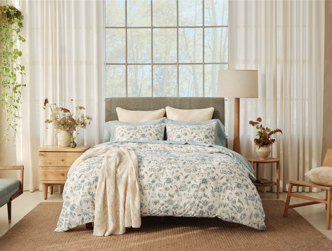Coyuchi Viola Print duvet cover styled on bed, blue floral pattern, with cream throw.