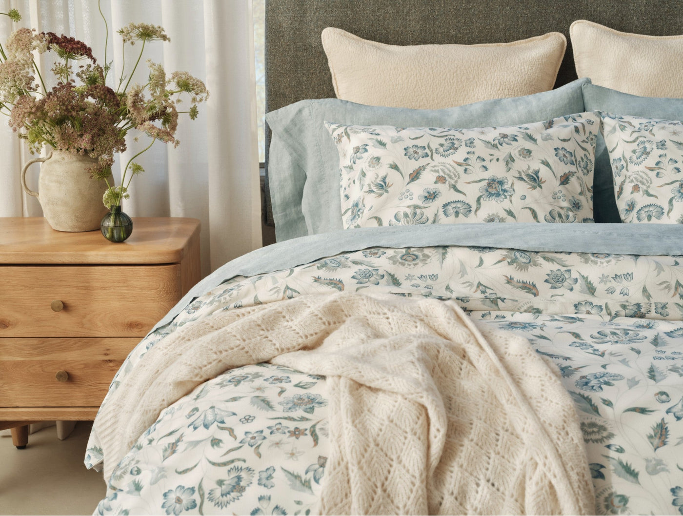 Viola Print sham in ivory with blue-green floral pattern, styled on bed with linen shams.