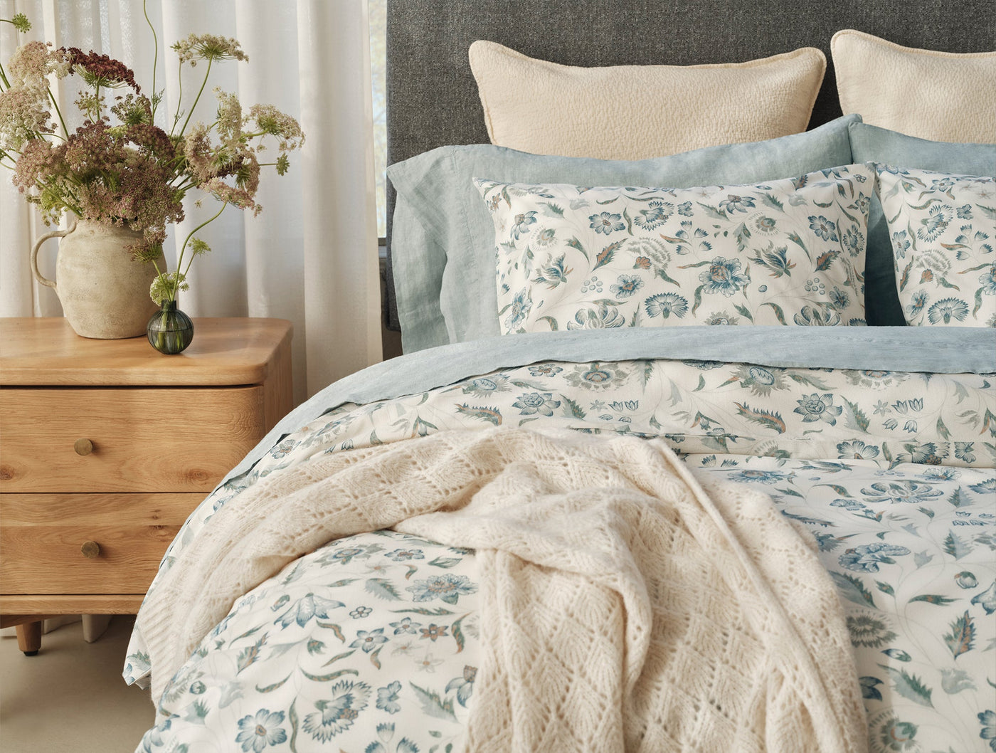 Coyuchi Viola Print duvet cover styled on bed with cream knit throw draped across foot.