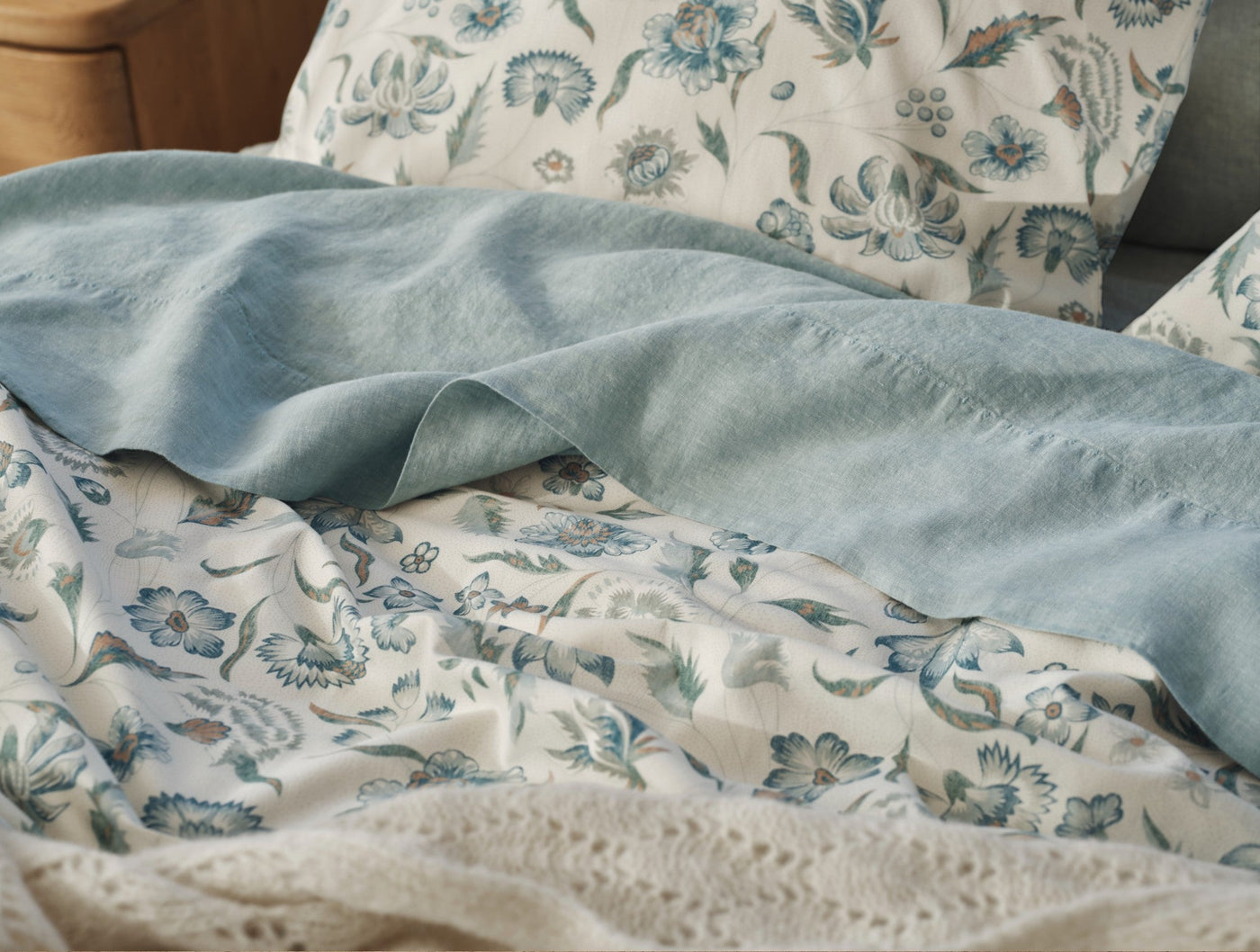Dusty blue linen layer over ivory Viola floral duvet, close-up of draped bedding.