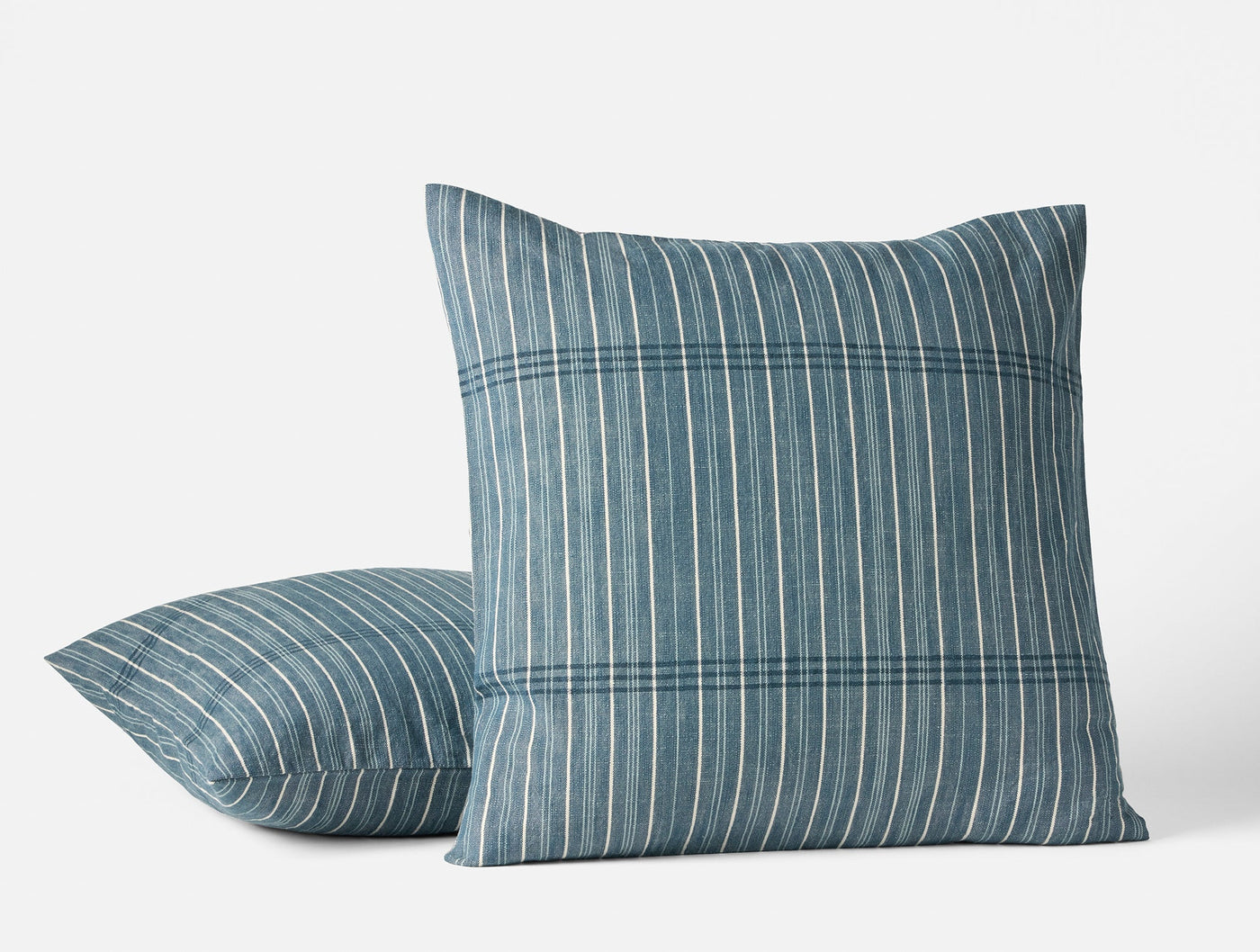 Two Coyuchi Fernwood pillows in slate blue with multi-stripe woven pattern, front and side view.