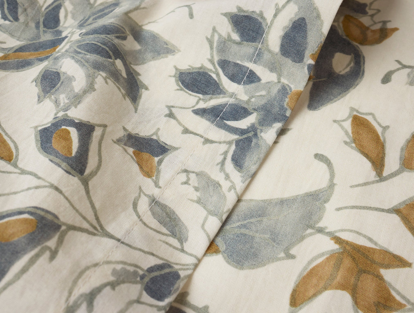 Close-up of Coyuchi Flora Print napkin fabric showing blue, gold, and grey botanical print.