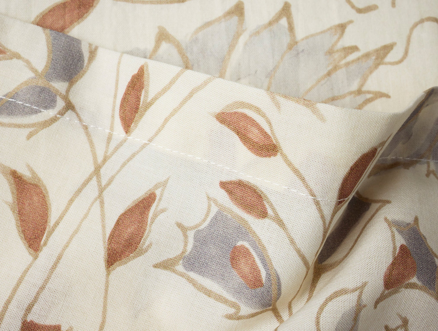 Close-up of Coyuchi Flora Print napkin hem, ivory fabric with terracotta and slate floral print.