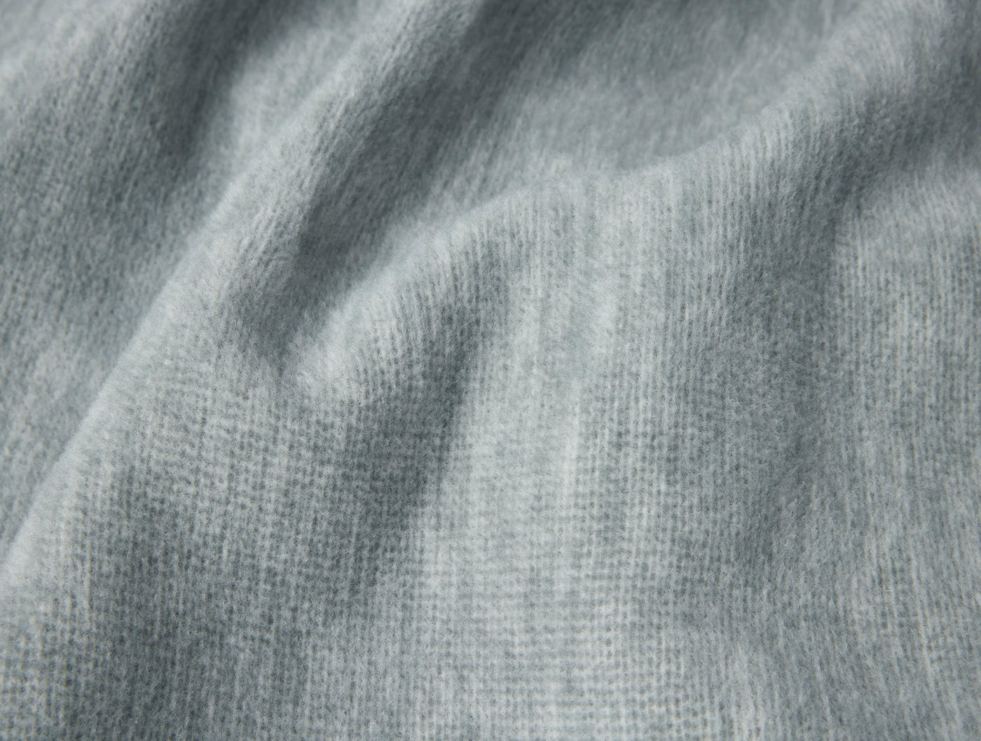 Close-up of Coyuchi Full Circle Cotton Blanket in mist grey, showing soft draped knit texture.