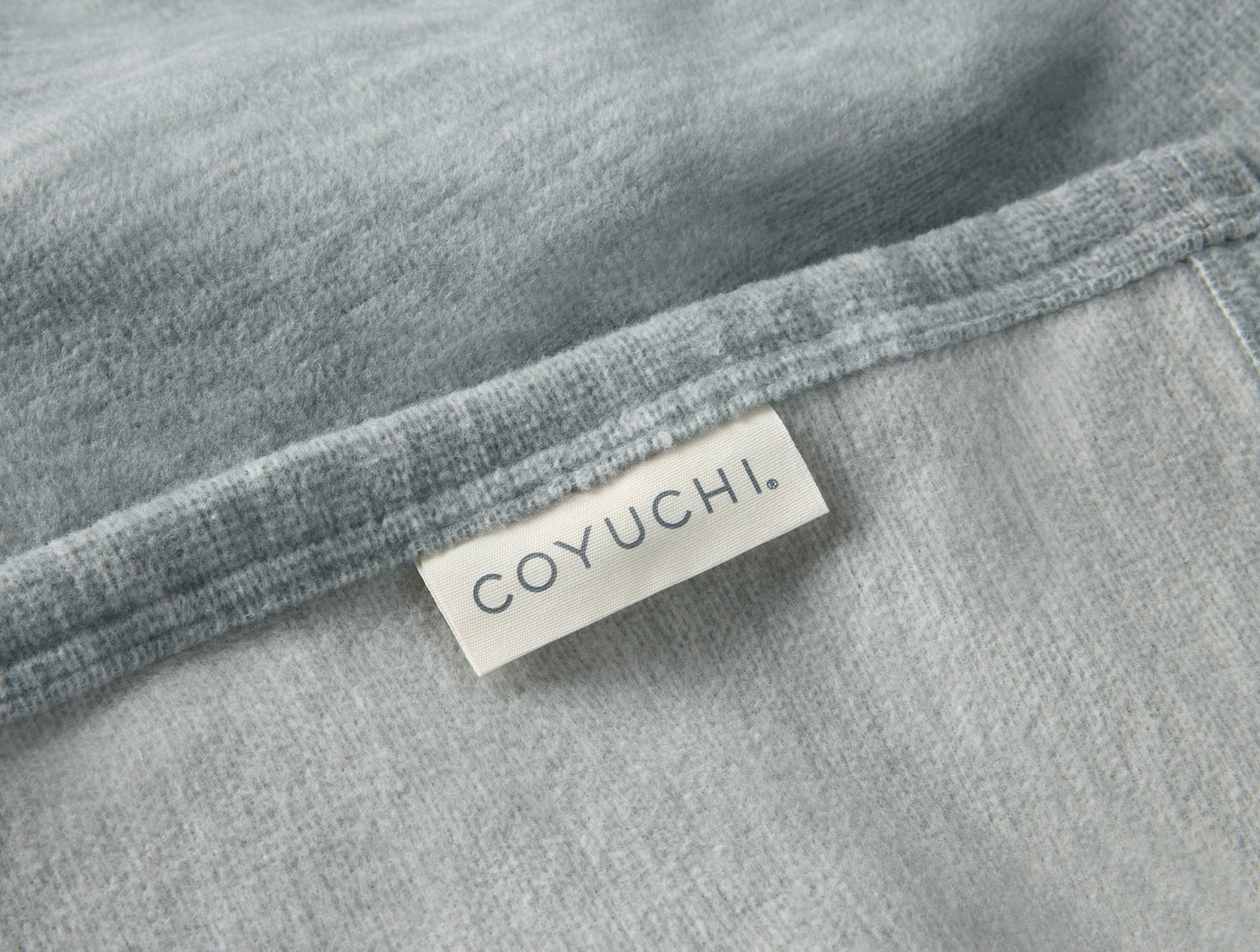 Close-up of Coyuchi label sewn onto a slate blue cotton blanket hem.