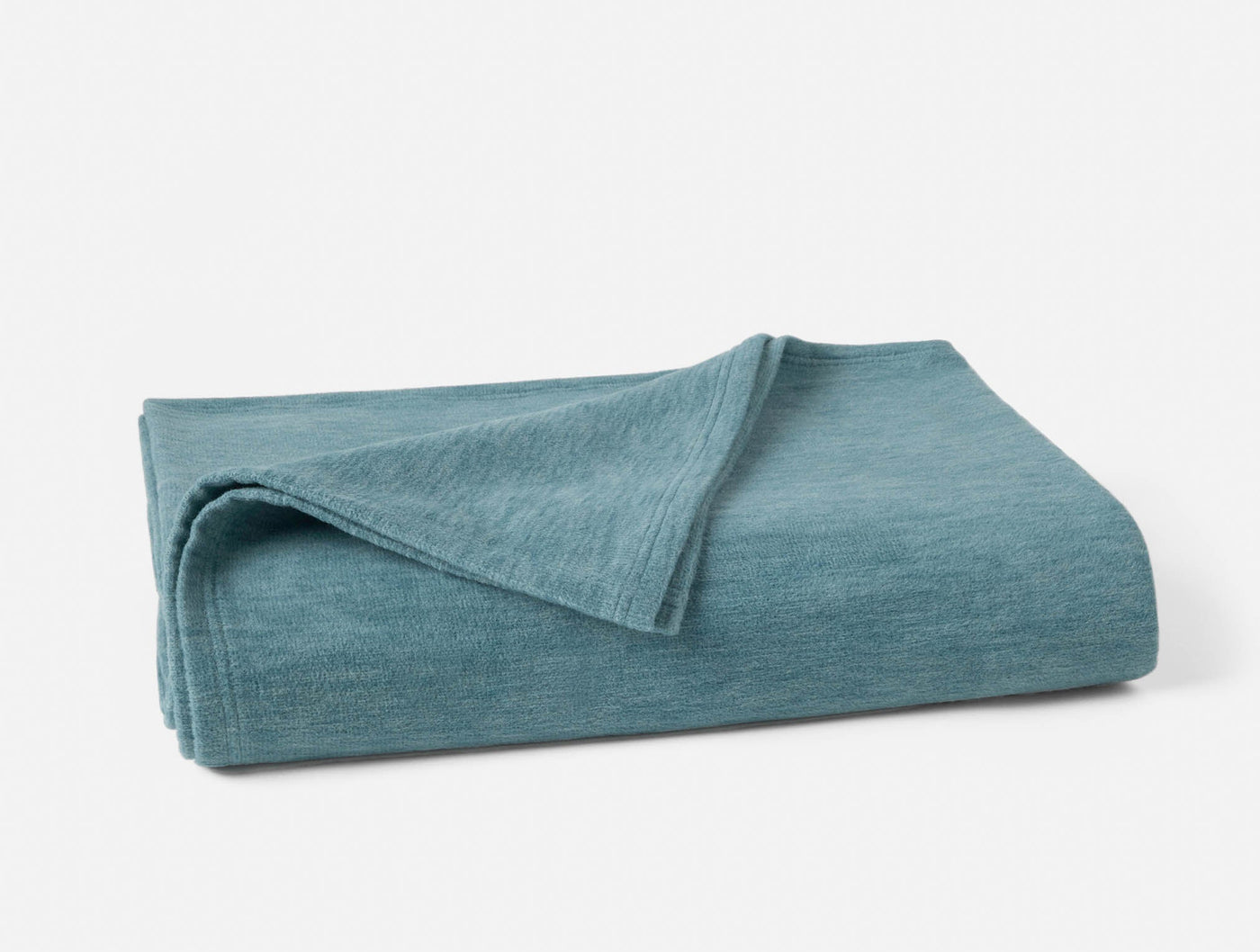 Coyuchi Full Circle Cotton blanket folded, showing teal heathered texture and corner detail.