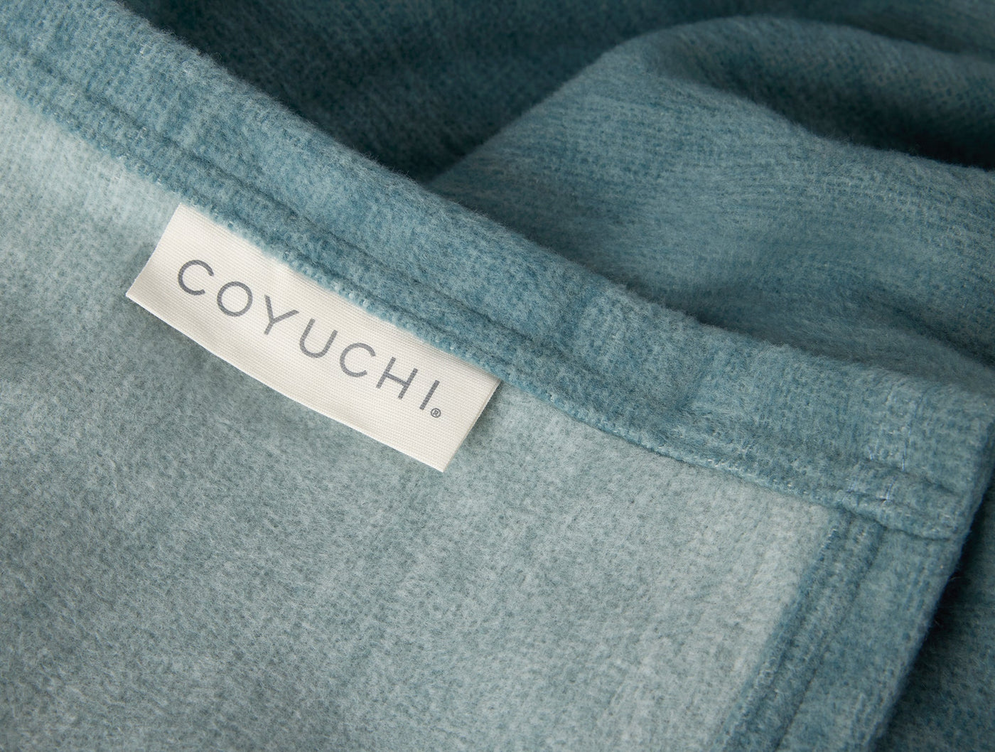 Close-up of Coyuchi label on folded teal cotton blanket hem.