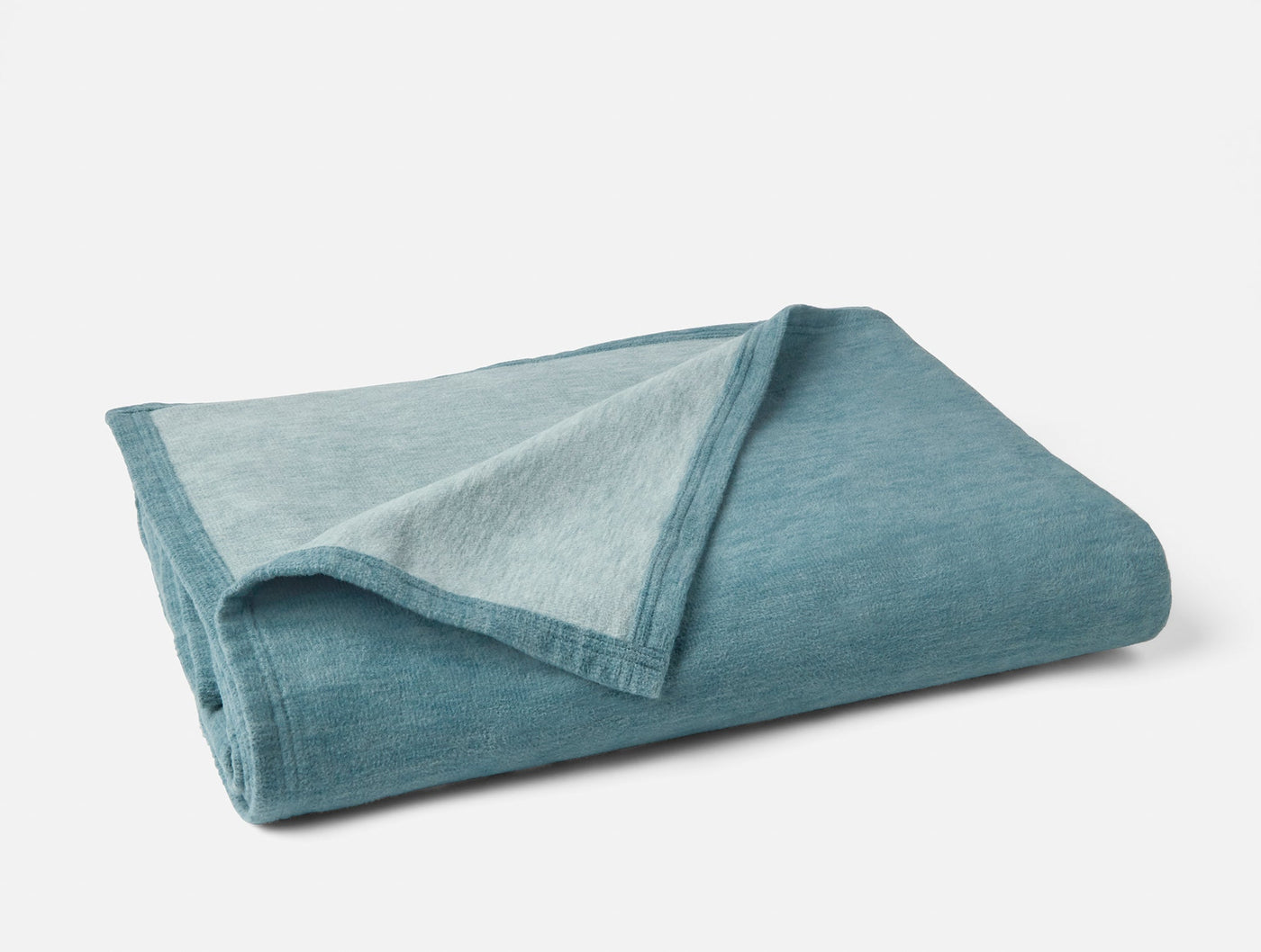 Folded teal cotton blanket showing contrast between deeper exterior and lighter reverse side.