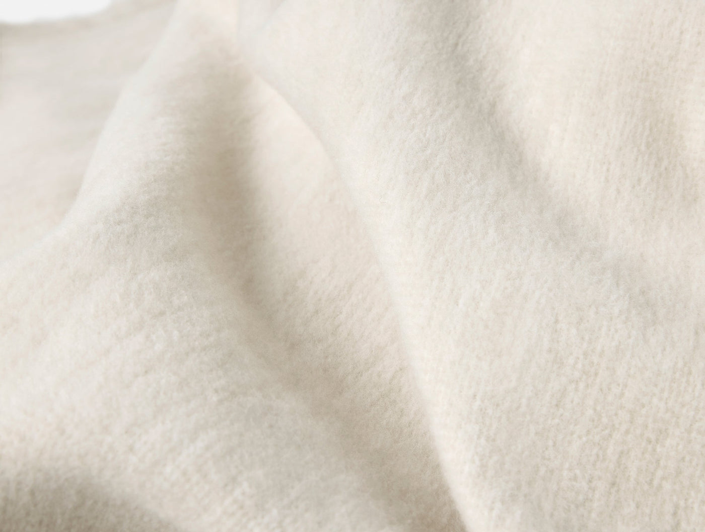 Close-up of ivory organic cotton blanket fabric showing soft, brushed texture and natural drape.