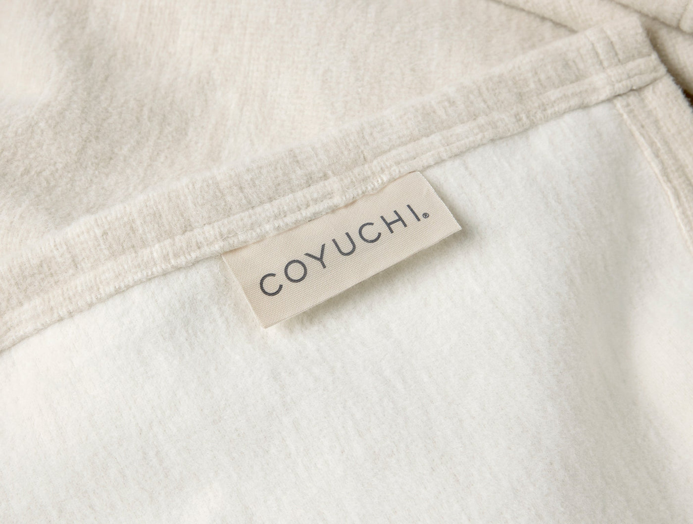 Close-up of Coyuchi woven label on folded ivory cotton blanket hem.