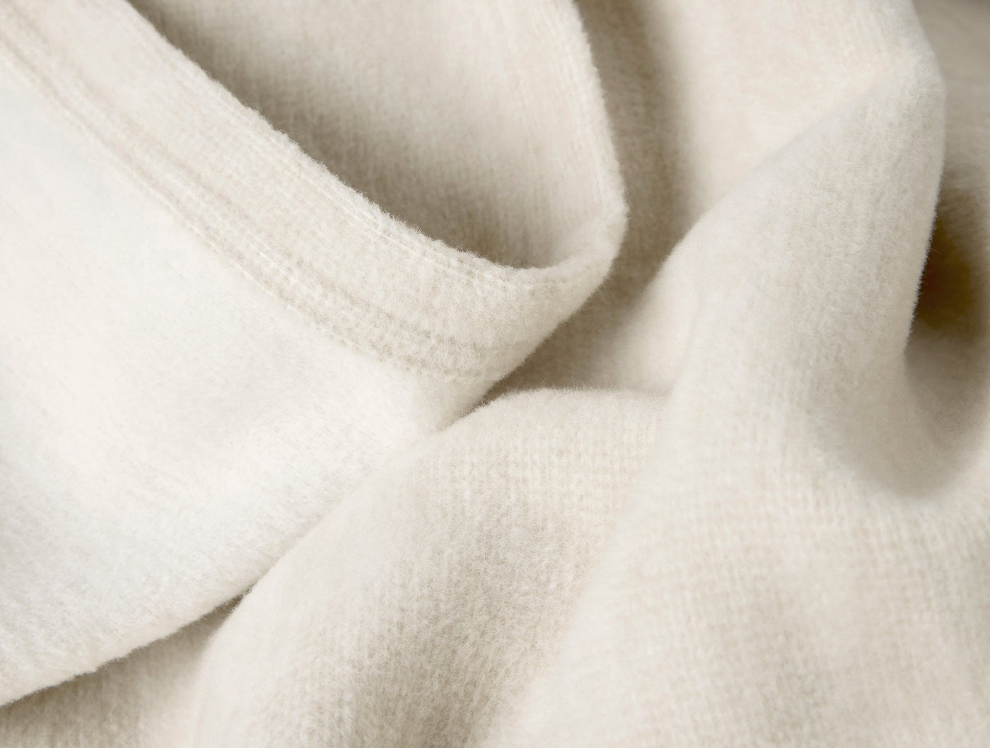 Close-up of ivory organic cotton throw fabric showing soft texture and folded hem detail.