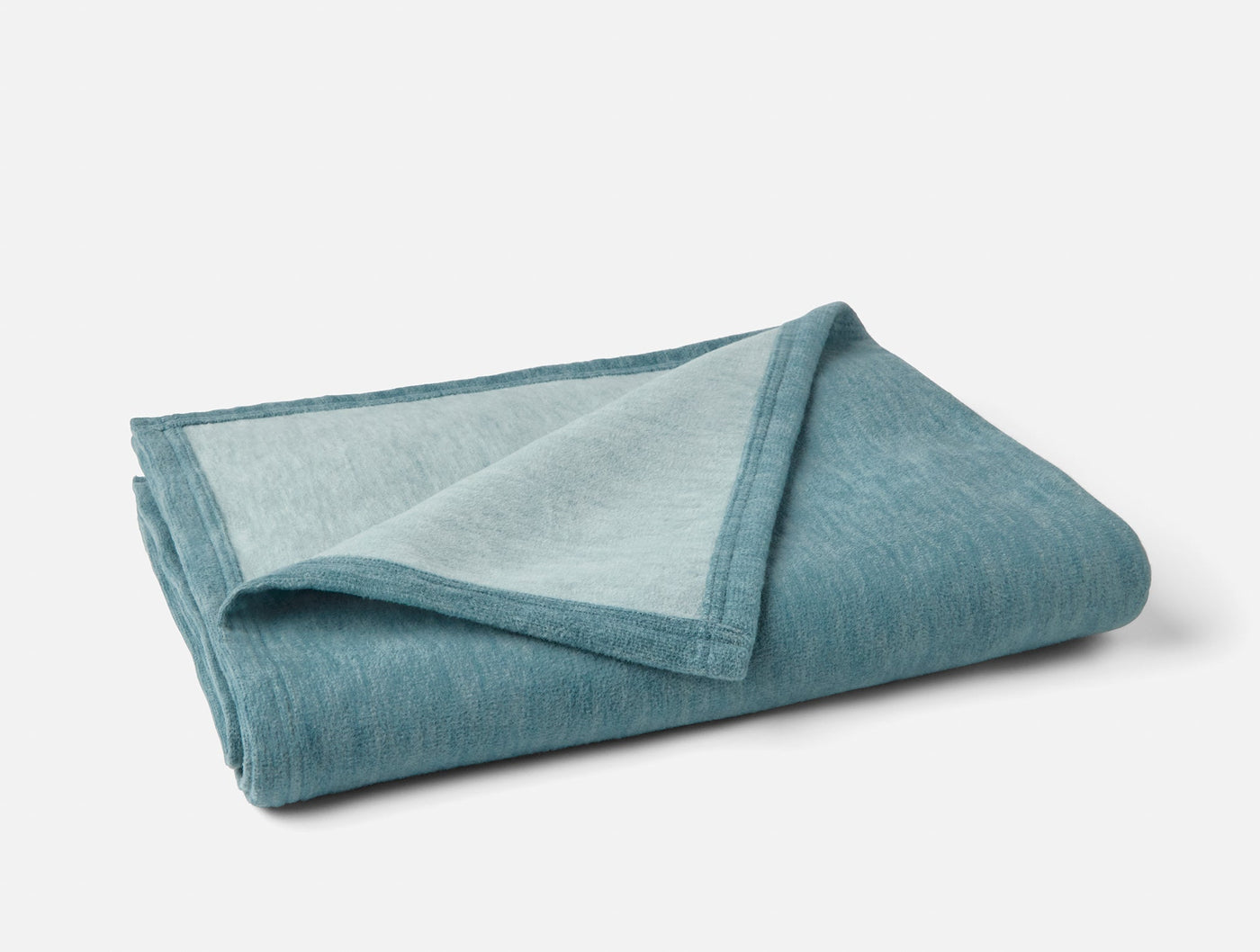 Folded Coyuchi throw in teal, showing two-tone reversible cotton weave.