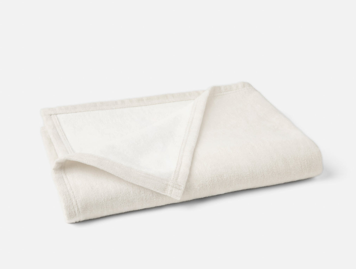 Close-up of folded ivory Coyuchi Full Circle Cotton Throw showing hem detail and woven texture.