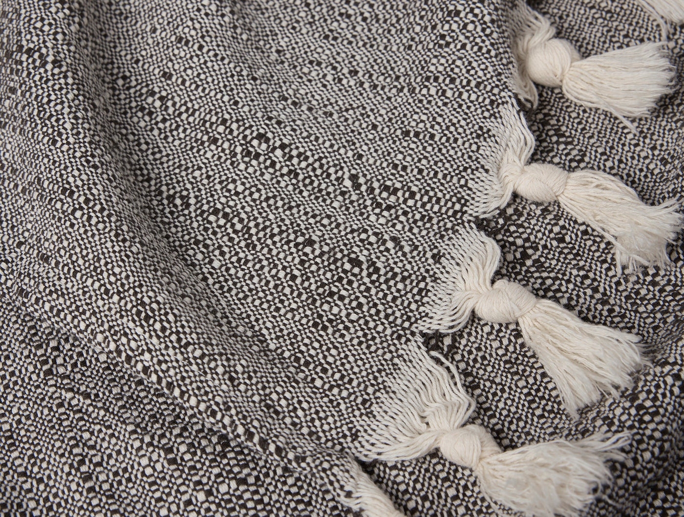 Close-up of Coyuchi Lido throw's charcoal woven texture with ivory knotted tassel fringe detail.