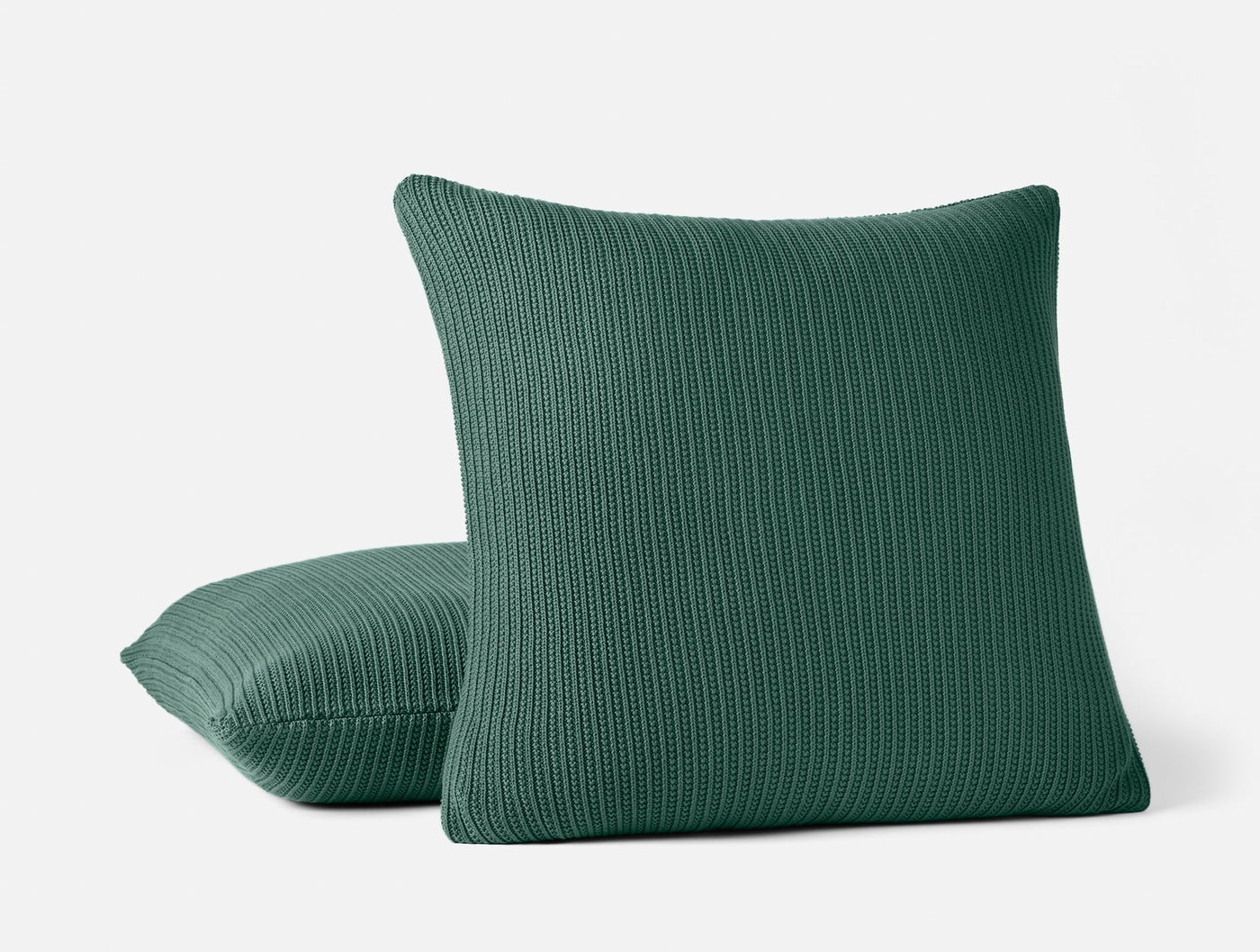 Two Coyuchi Linea Knit pillows in forest green with ribbed texture, stacked against white background.